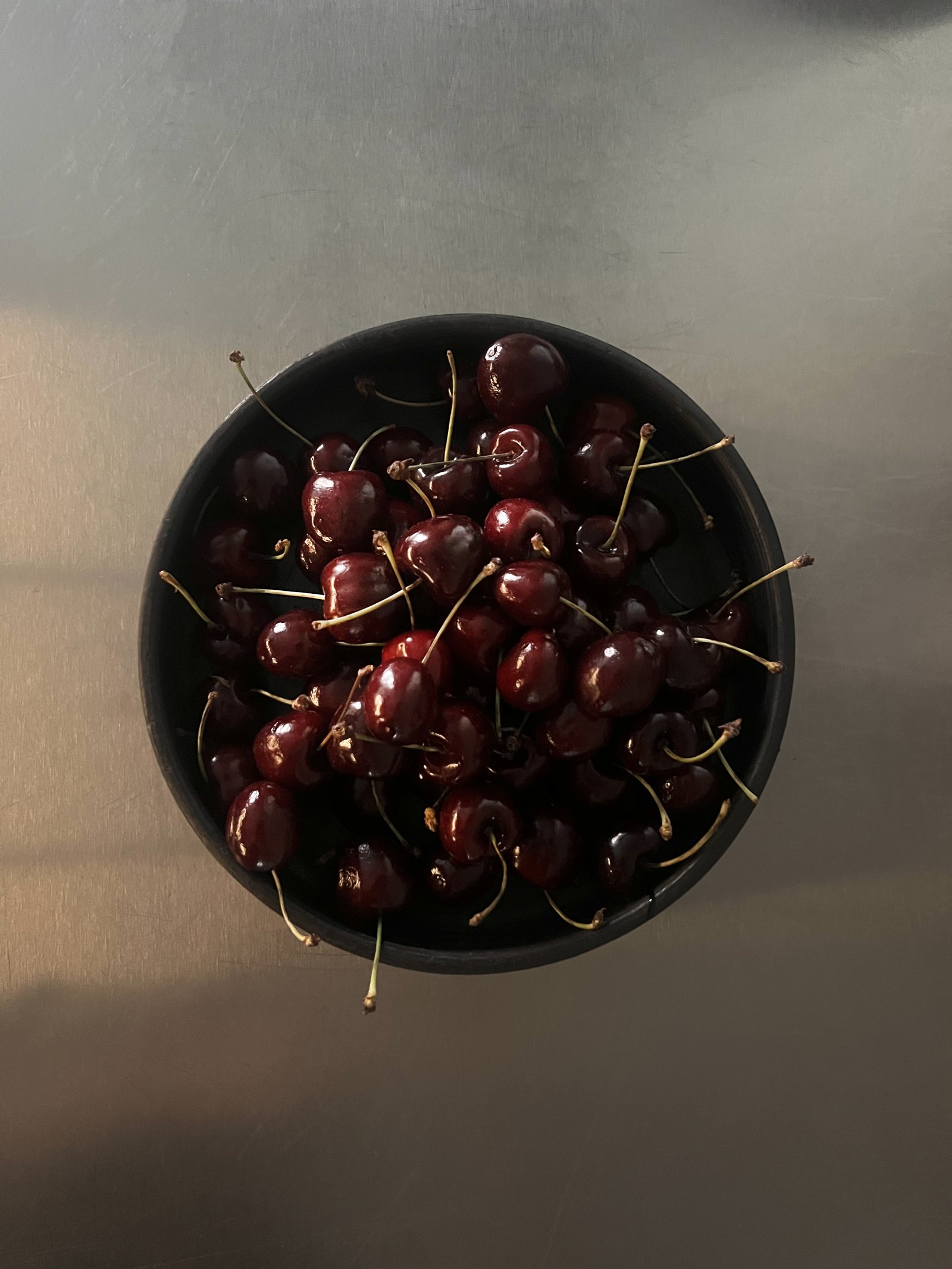 Cherries in a dark clay bowl, window light